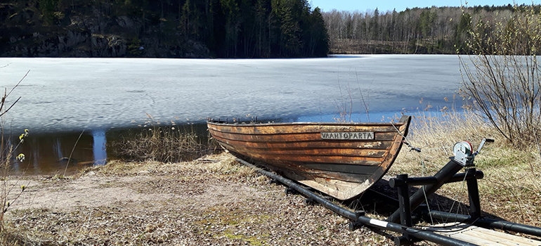 Holzboot liegt an einem Seeufer mit Blick auf Wald und Wasser.