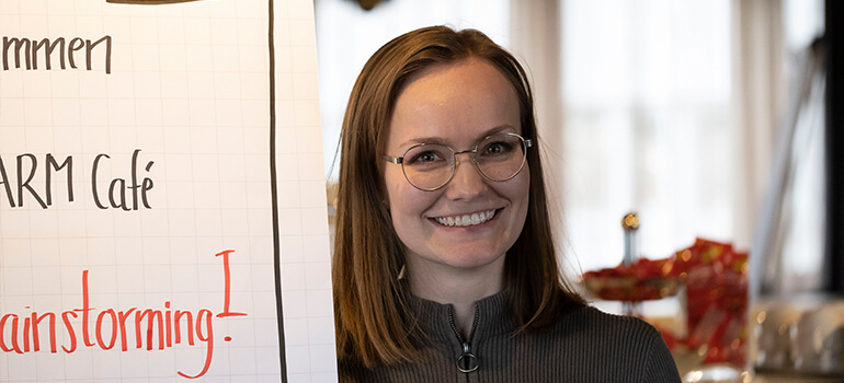 Frau lächelt in die Kamera, im Hintergrund ein Flipchart mit der Aufschrift Brainstorming.